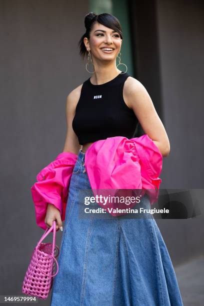 Elisa Maino is seen wearing circle gold pendant earrings, a MSGM black cropped tank top with white lettering, a light blue denim maxi skirt, a bright...