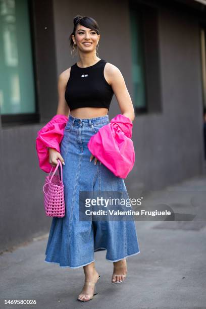 Elisa Maino is seen wearing circle gold pendant earrings, a MSGM black cropped tank top with white lettering, a light blue denim maxi skirt, a bright...