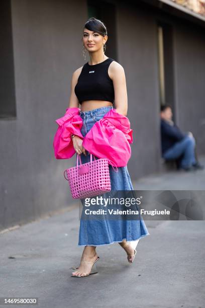 Elisa Maino is seen wearing circle gold pendant earrings, a MSGM black cropped tank top with white lettering, a light blue denim maxi skirt, a bright...
