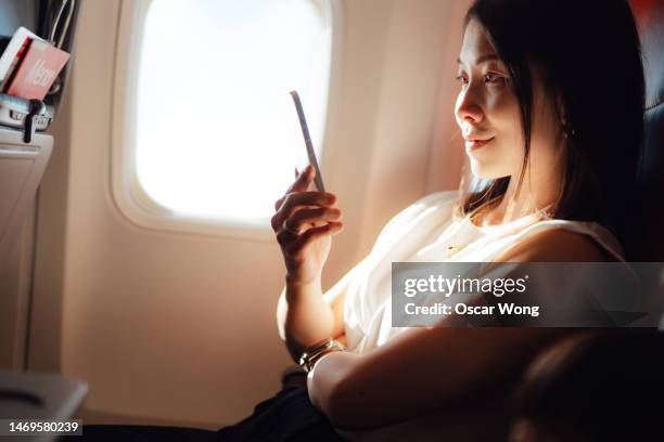 young asian business woman using smartphone while sitting on the plane - airport lights stock pictures, royalty-free photos & images