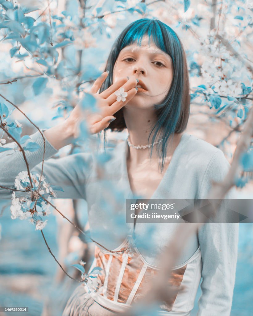 Asian woman with blue hair on the background of a flowering tree. Bang hairstyle. Spring garden. White flowers