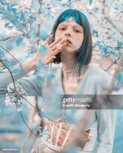 asian woman with blue hair on the background of a flowering tree. bang hairstyle. spring garden. white flowers - fee stockfoto's en -beelden