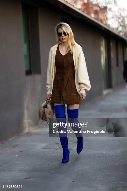 Guest is seen wearing black sunglasses, a white cream wool cardigan, a brown suede mini dress, bright-blue over the knee boots and a puffy fur brown...