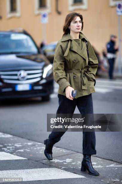 Guest is seen wearing silver earrings, a kaki short belted trench with black bottoms, a black leather bag, black denim jeans and black leather ankle...