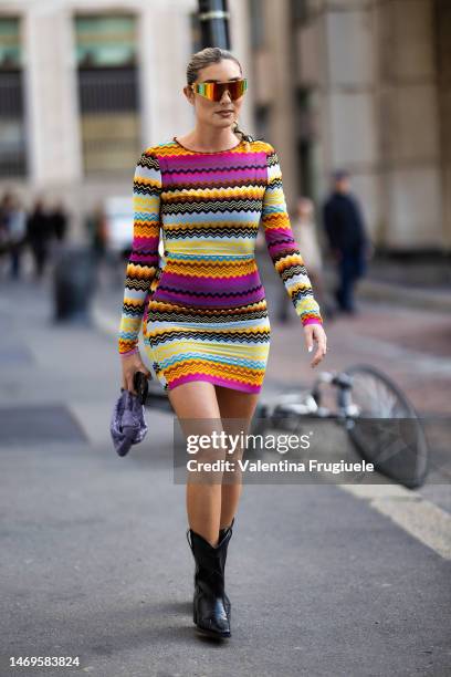 Guest is seen wearing opalescent sunglasses, a mini multicolored dress, a Bottega Veneta lilac handbag and black leather cow-boy boots outside the...