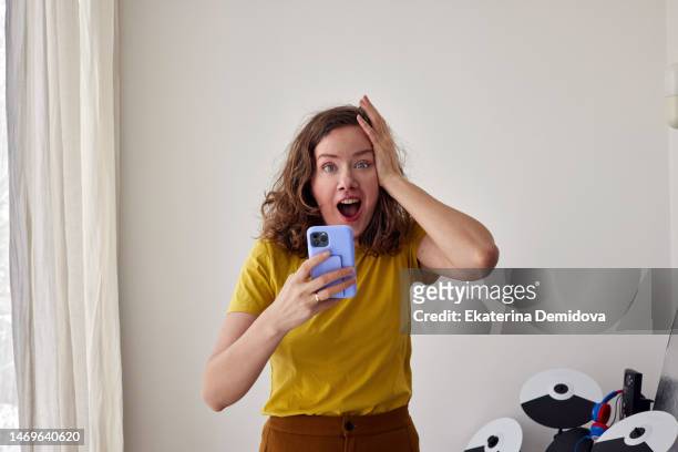curly woman with smartphone in shock holding her head on white background - awards inside stockfoto's en -beelden