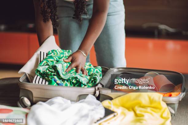 african american woman stacking clothes and shoes into bag case, trying to pack hand luggage - suitcase packing stockfoto's en -beelden