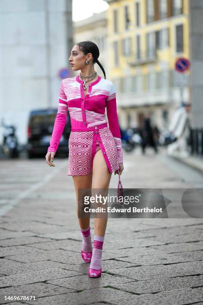 Ginevra Mavilla wears silver earrings, a silver large chain necklace, a neon pink and white bicolored print pattern buttoned cardigan, a matching...