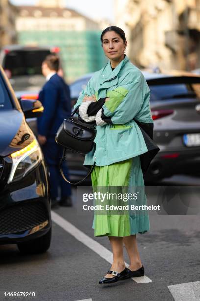 Caroline Issa wears gold pendant earrings, a black t-shirt, a pale blue and green print pattern oversized jacket, a matching pale blue and green...