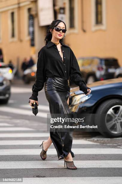 Chriselle Lim wears black sunglasses, a gold necklace, silver small earrings, a black buttoned V-neck shirt, a black shiny clutch , a black shiny...
