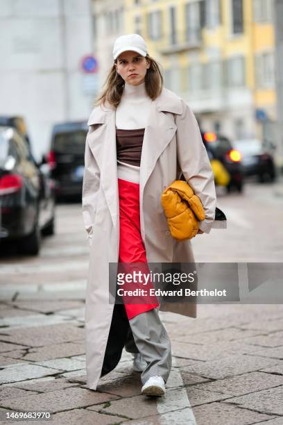 Guest wears a white cap, a beige turtleneck t-shirt, a brown cropped tank-top, a beige oversized long coat, a yellow mustard shiny leather puffy...