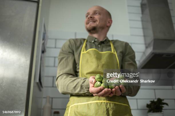smiling man holding brussels sprouts in his hands and groaning - handvol stockfoto's en -beelden