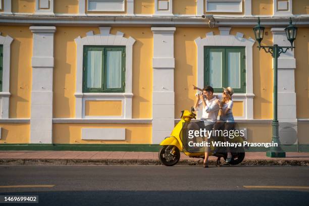 a young couple rides a scooter in bangkok and has fun - holiday scooter fotografías e imágenes de stock