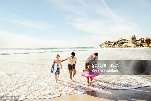 happy family, kids or beach running with inflatable, ocean wakeboard or fun in game, energy or bonding. children, playing or water sea toys and interracial parents in freedom holiday or summer travel - mother and child in water at beach stock pictures, royalty-free photos & images