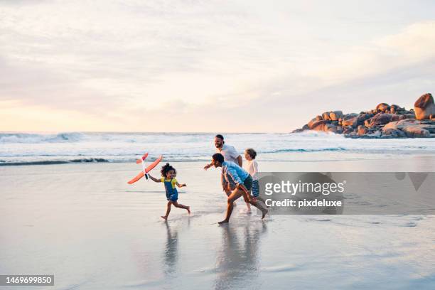 happy family, running or flying toys on sunset beach or ocean in freedom holiday, energy bonding or travel playing fun. sea, children or kids with airplane, interracial parents or aeroplane by nature - vacation stockfoto's en -beelden