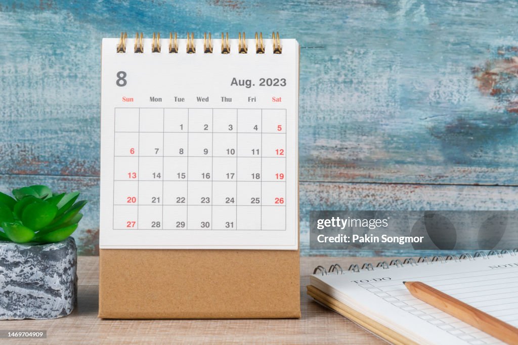 Calendar Desk 2023: August is the month for the organizer to plan and deadline with a houseplant and note pad against an old wooden table background.