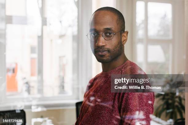 portrait of young office employee behind window pane - portrait of pensive young businessman wearing glasses stock-fotos und bilder