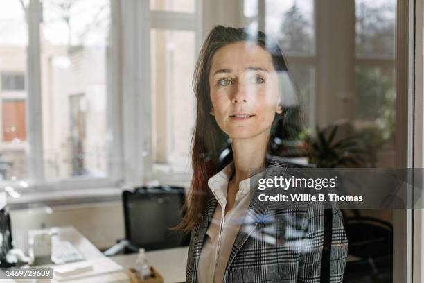 businesswoman looking through window pane in office - einzelne frau über 40 stock-fotos und bilder