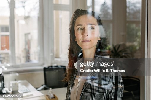 Businesswoman Looking Through Window Pane In Office Businesswoman Looking Through Window Pane In Office