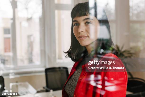 businesswoman wearing red shirt standing behind glass window - contemplation window stock-fotos und bilder