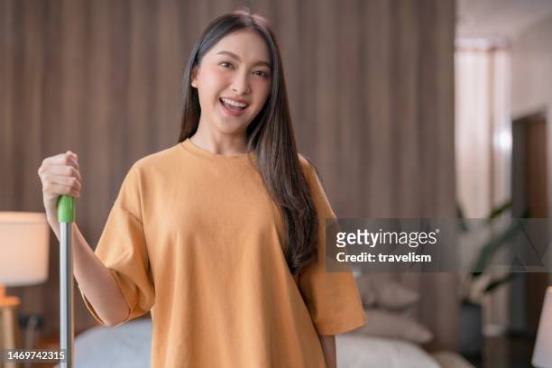 young asia female woman working in her new house. she is cleaning the floor with a mop at her apartment,asian maid clean up room with mop in apartment or home with happy and funny mood at living room - holding broom stock pictures, royalty-free photos & images