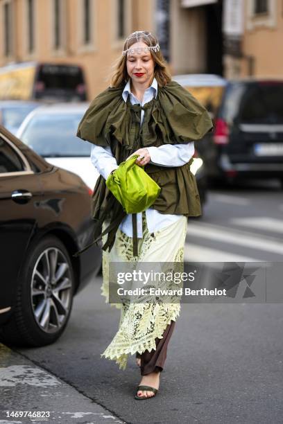 Guest wears a white pearls checkered and crystals pendant hat, a pale blue shirt, a khaki puffy short sleeves blouse, a green silk handbag, a pale...