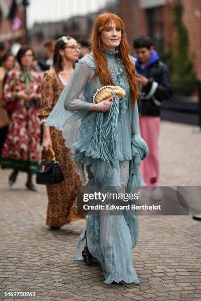 Florence Welch wears a gray blue pleated / accordion high neck / bat sleeves / long ruffled dress, a beige pearls and white handbag clutch with blue...