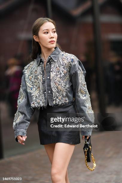 Jenny Suet In Tsang wears silver chain necklaces, a gray denim with embroidered silver with embroidered pearls pattern buttoned cropped jacket, a...
