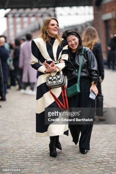 Anna Dello Russo wears silver earrings, a black turtleneck pullover, a black and white latte striped print pattern shoulder-pads long dress, a black...