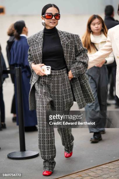 Yoyo Cao wears black and red sunglasses, a silver large earrings, a black turtleneck wool pullover, a gray and white rhinestones checkered print...