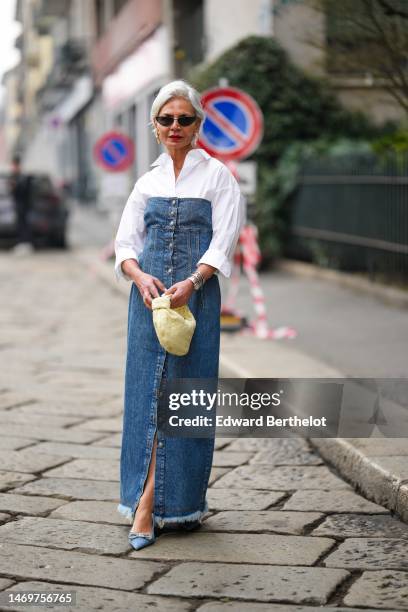 Grece Ghanem wears black vintage sunglasses, white pearls pendant earrings, a blue denim shoulder-off / buttoned long ripped dress, a pale yellow...