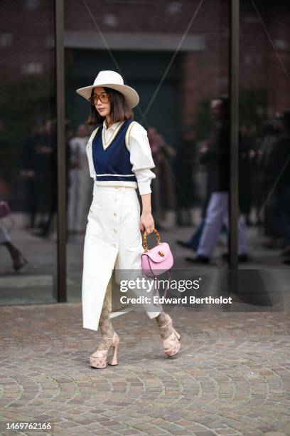 Guest wears a white felt wool hat, orange sunglasses, a white puffy shoulder shirt, a navy blue with white large borders V-neck / sleeveless...