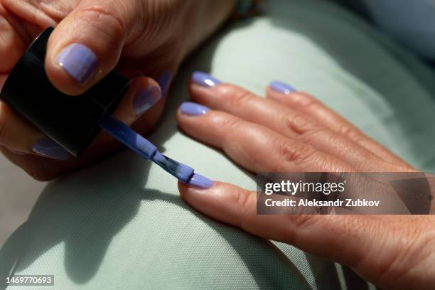 a high school student does a manicure. a woman paints her nails with nail polish in a bright color. an independent manicure in the open air, and not from a cosmetologist. do it yourself. body care during your stay at home, during closed beauty salons. - painting toenails stock-fotos und bilder