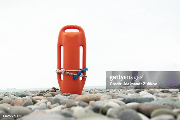 lifeguard float or lifeline, on the sand or pebbles of the beach, on the seashore. the end of alexandrov. an item for saving drowning people. the coastline, the water's edge. the concept of safety, saving people's lives. - red guards stockfoto's en -beelden