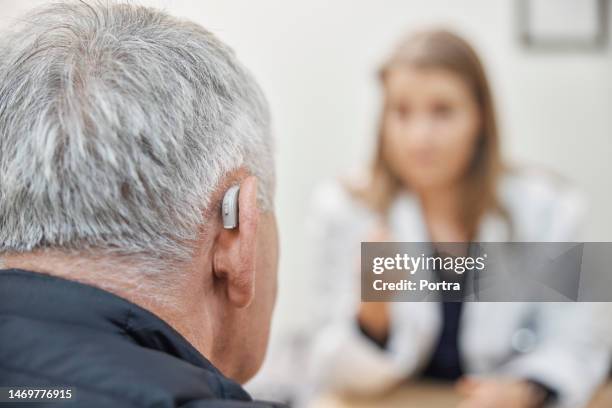 close-up of a senior man with hearing aid visit his doctor at clinic - hearing aids stock pictures, royalty-free photos & images