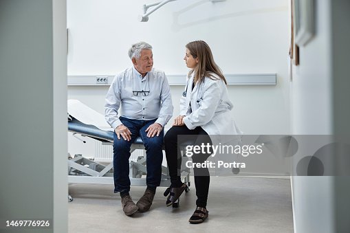 Reifer Patient spricht mit Arzt, während er in der Klinik auf dem Bett sitzt Reifer Patient spricht mit Arzt, während er in der Klinik auf dem Bett sitzt