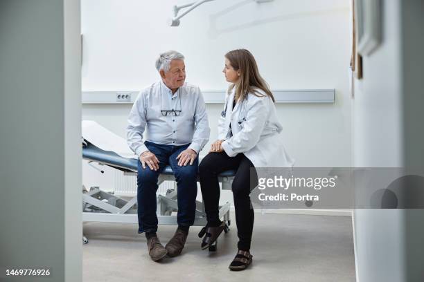 reifer patient spricht mit arzt, während er in der klinik auf dem bett sitzt - arzt stock-fotos und bilder