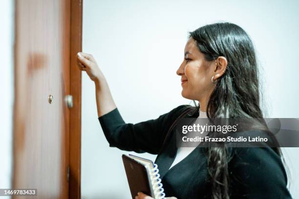 young woman knocking on the door of a home - knocking stockfoto's en -beelden