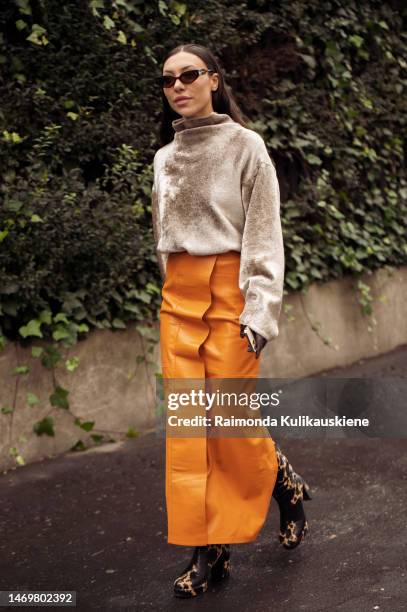 Guest is seen wearing light beige shiny sweater, long orange leather skirt, golden mini bag, and black and brown shoes outside the Annakiki show...