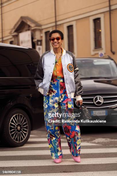 Tamu McPherson is seen wearing orange sunglasses, gold circle earrings, a beads necklace, a silver and grey basketball jacket with patches on it, an...