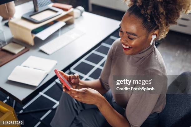 une belle femme d’affaires heureuse avec des cheveux blonds bouclés utilisant ses écouteurs tout en regardant quelque chose sur son téléphone portable - in ear headphones photos et images de collection