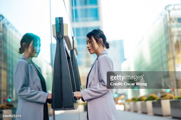 young business woman withdrawing cash at automatic cash machine (atm) in the city - atm stock pictures, royalty-free photos & images