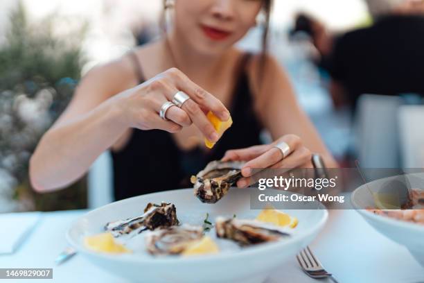 close-up of woman's hand squeezing lemon juice on fresh oysters - ostrica foto e immagini stock