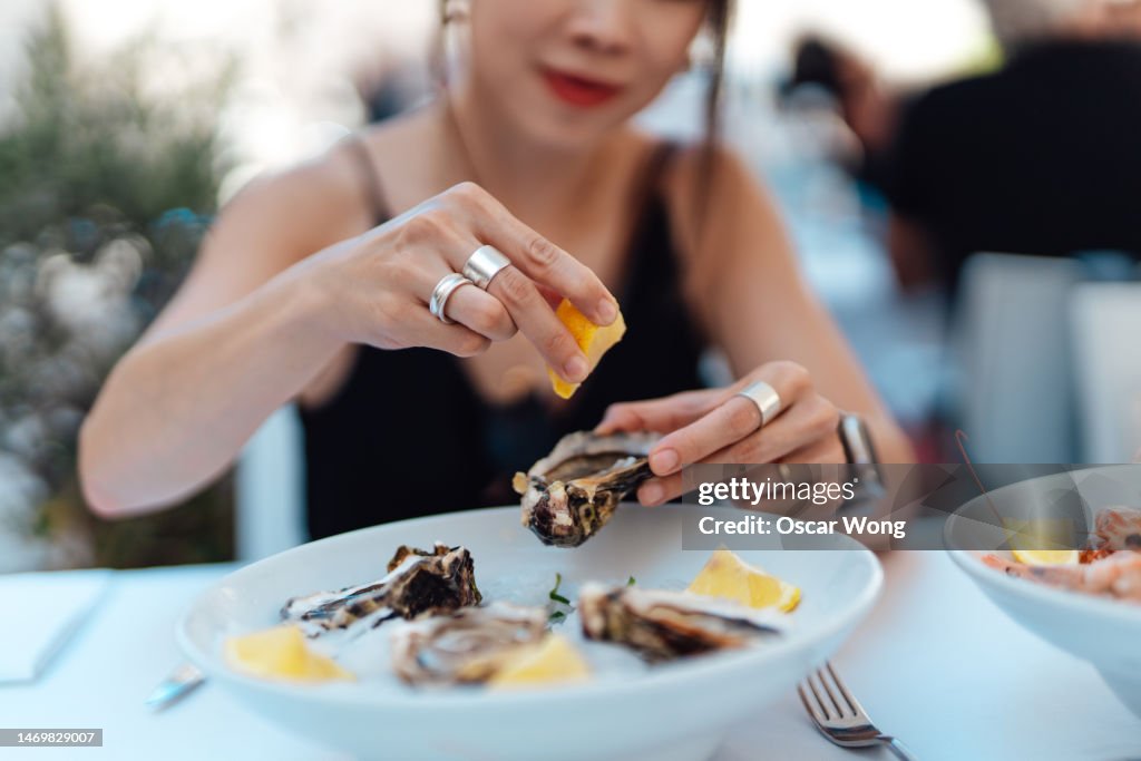 Close-up of woman's hand squeezing lemon juice on fresh oysters