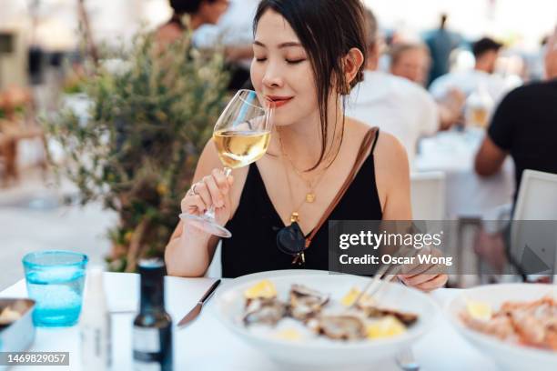 young asian woman drinking white wine while eating seafood at outdoor restaurant - incidental people stock pictures, royalty-free photos & images