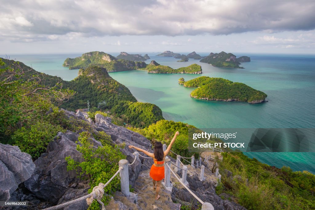 A woman walking on a staircase with mountain views and the emerald sea below and the weather was thick with clouds like it was going to rain