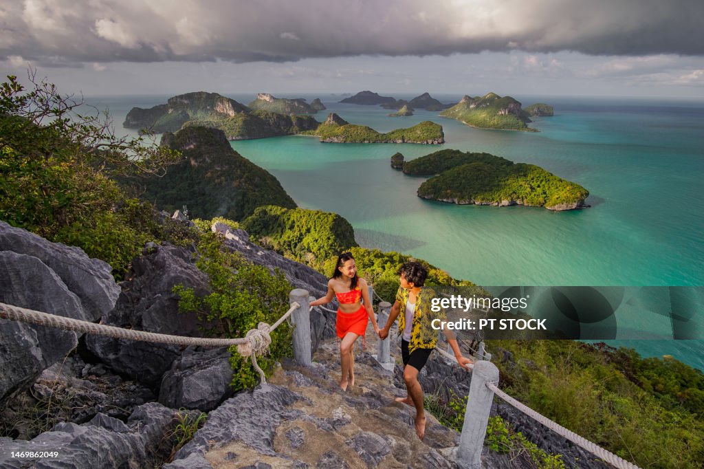 A man and a woman walking on stairs overlooking the mountains and the emerald sea below. and the air was overcast, as if it was about to rain.