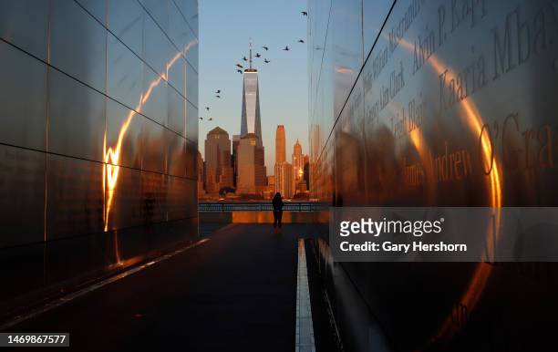 The sun sets on lower Manhattan and One World Trade Center in New York City as people walk through the Empty Sky 9/11 Memorial in Liberty State Park...