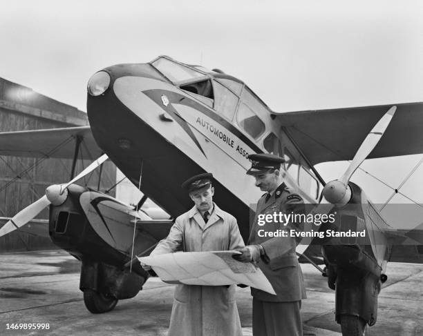 British pilots Captain Donald Whitehead and Captain Bill Lewis inspecting a map as they stand in front of biplane airliner, de Havilland DH 89 Dragon...