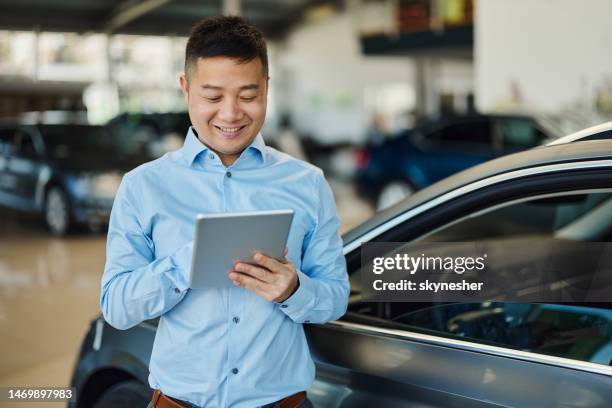 happy asian salesman using touchpad in a car showroom. - car dealership stock pictures, royalty-free photos & images